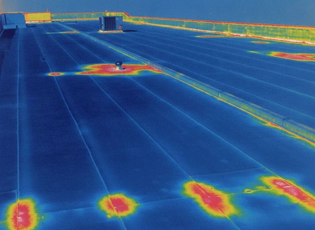Thermal image of a flat roof with saturated areas glowing warm against cool dry field