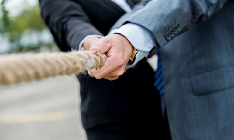 two individuals from different businesses having friendly competition in a game of tug of war